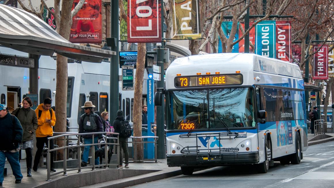 Passengers walk along light rail platform with bus in foreground. 