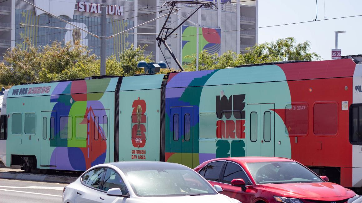 wrapped train with FIFA design, cars in foreground, stadium in background