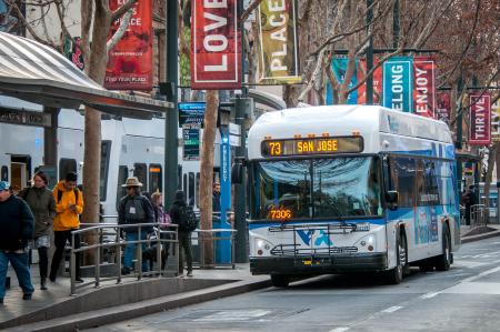 Passengers walk along light rail platform with bus in foreground. 