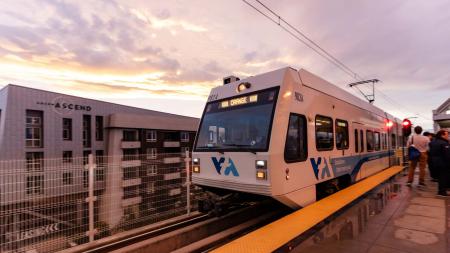 VTA light rail train driving on tracks next to a building