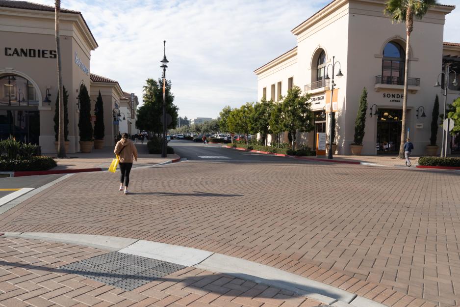 Photo of an intersection paved in brick with a woman walking across the street.