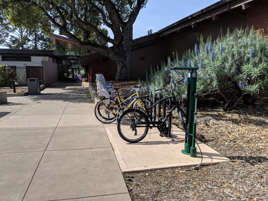 Photo of bicycle racks at the entrance of a library. Adult and children's bikes are parked at the rack.