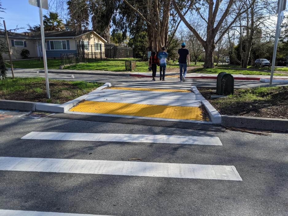 Photo of a midblock crossing with a pedestrian refuge island. People are using the crosswalk.