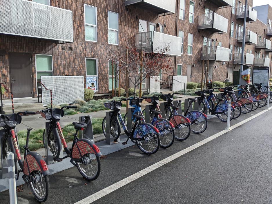 A photo of a bikeshare with 15+ bikes next to an apartment building.