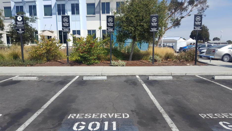 A photo of four parking spots reserved for car share program vehicles near a building's entrance. 