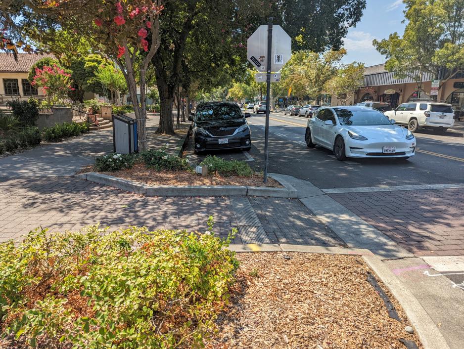 A photo of a sidewalk with a curb extension with a brick crosswalk.