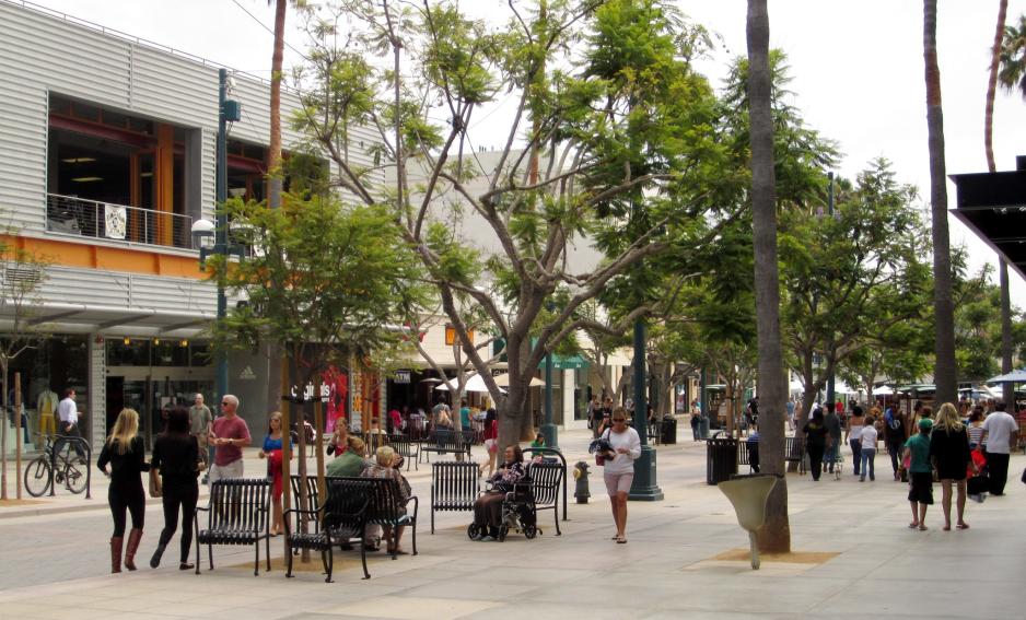 Photo of a pedestrian street in a commercial area. Street trees, benches, people walking, sitting, shopping.