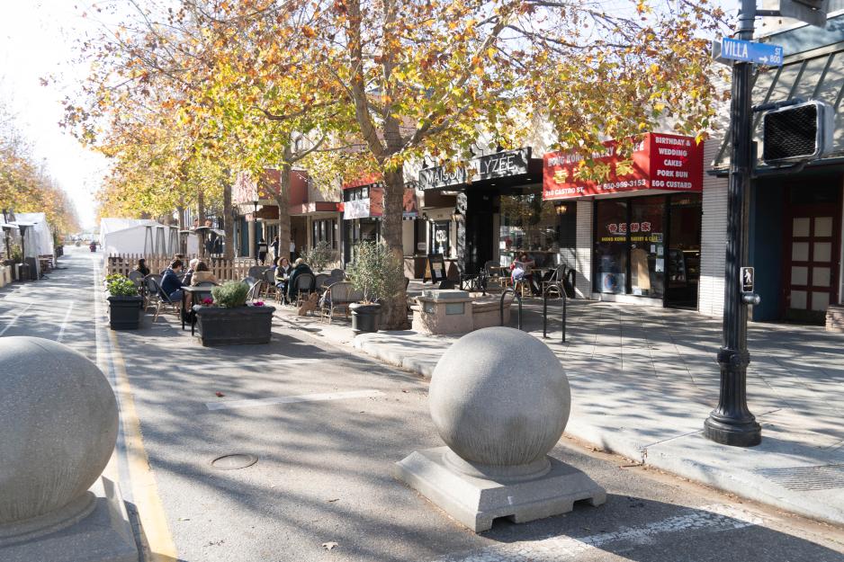 Photo showing Castro Street in Mountain View. Decorative concrete barriers block the street to traffic. Outdoor restaurant seating.