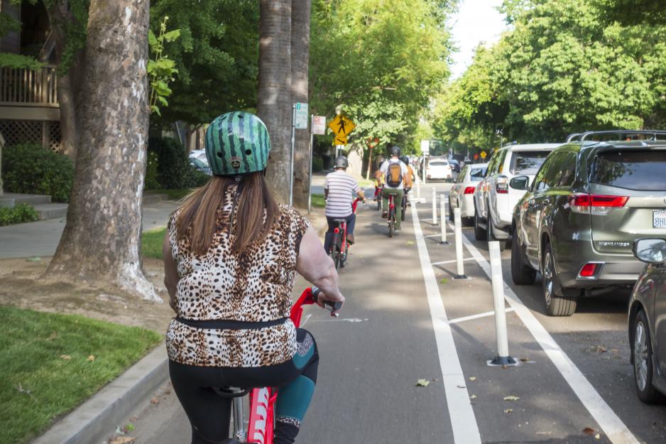 Photo from a bicyclists point of view of people biking in a bike lane protected from traffic by parked cars.