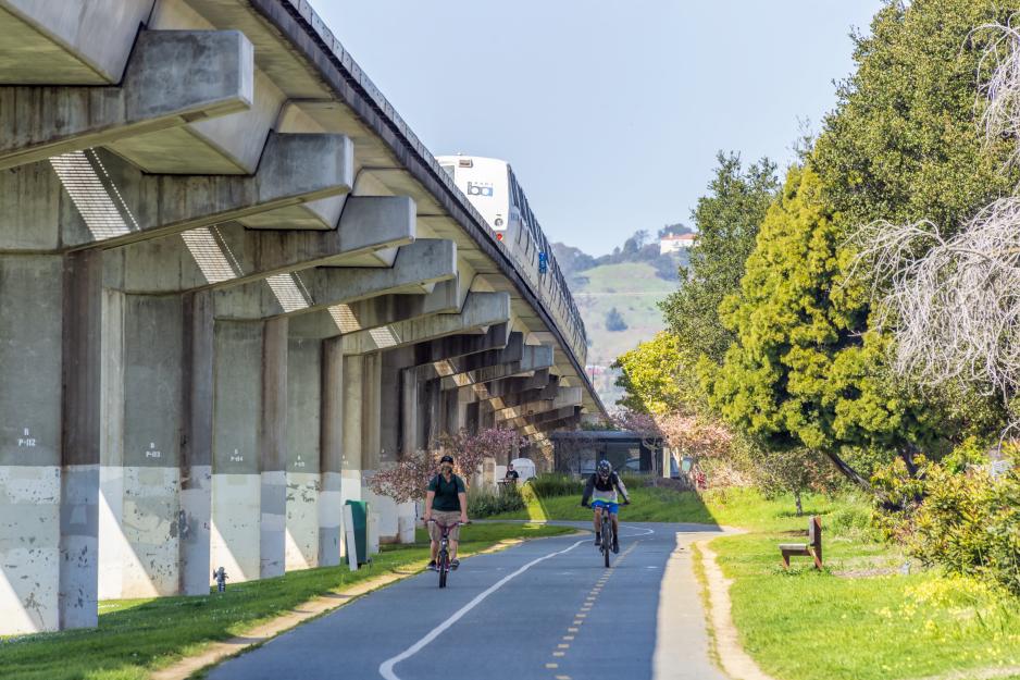 Photo of bike path adjacent to elevated BART guideway with people biking on it.