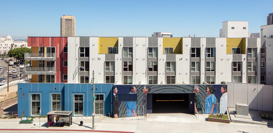 A photo of a parking garage next to a five story residential development. The parking garage has art and complements the color of the residential development. 
