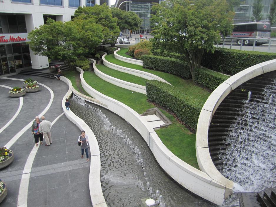 A photo of plaza near a cafe with elevated grass and a water feature. 