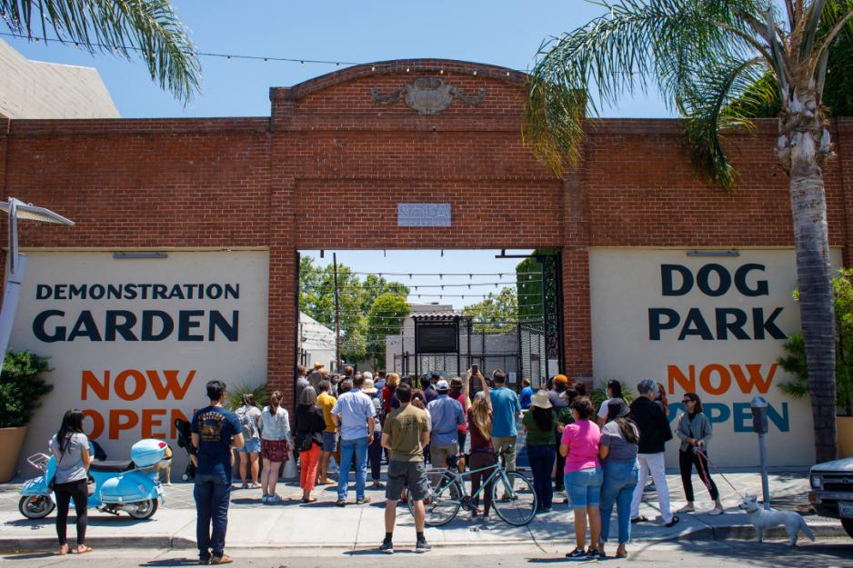 A photo of a people walking at a brick entrance with signs for a "garden demonstration" and "dog park."