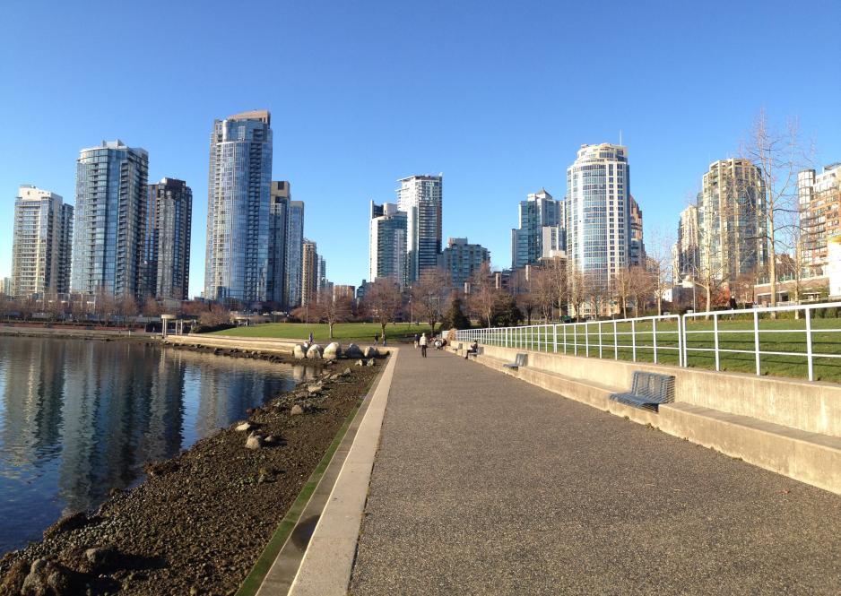 A photo of a walking trail next to a body of water and near high rise buildings. 