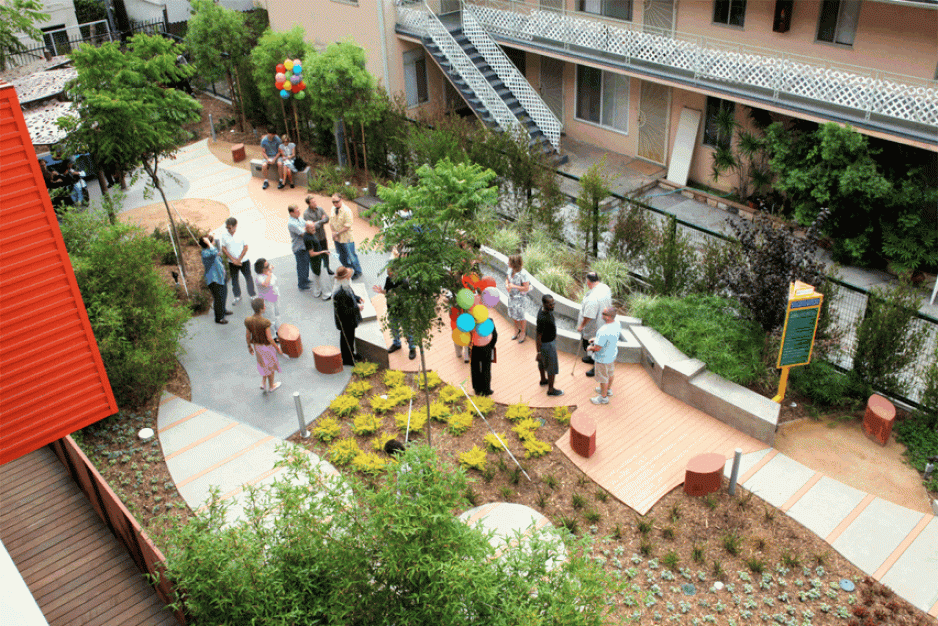 An photo of a small park in between two buildings with seating, plants, and trees.