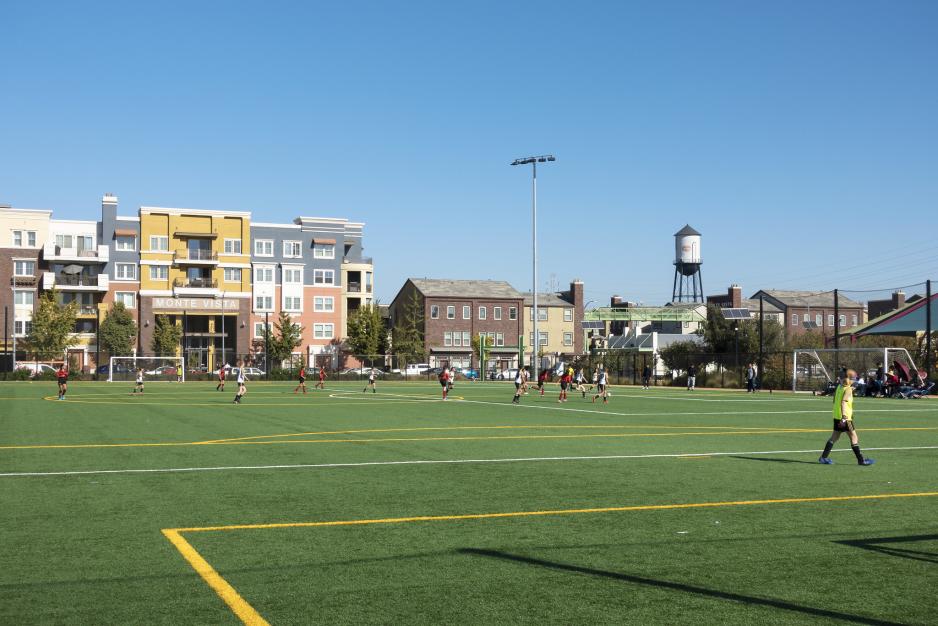 A photo of children playing at a soccer field next to an apartment building.