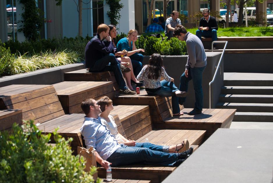 A photo of a people sitting in a plaza on wooden step seating.