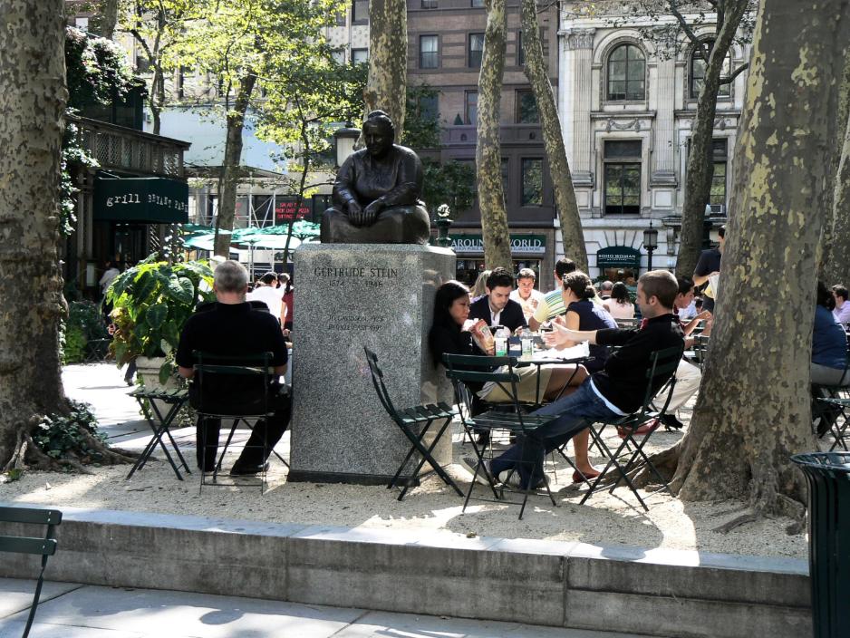 A photo of people sitting on chairs/tables in a plaza. 