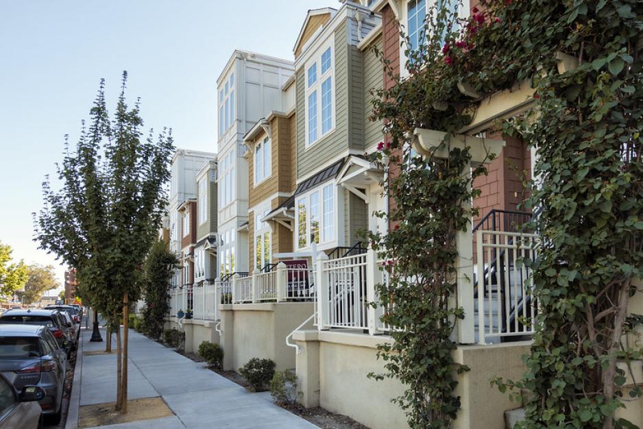 A photo of a row of townhouses with a sidewalk, street trees, and parallel parking