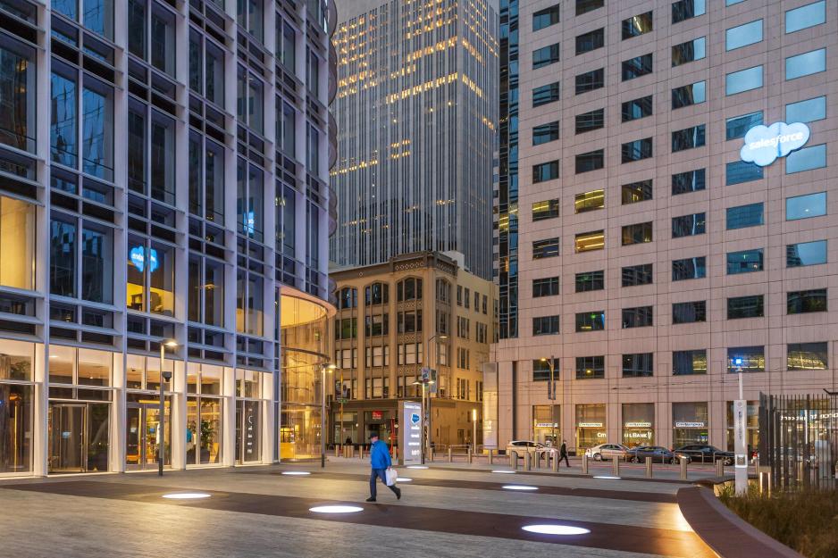 A photo of a plaza in front of a high-rise building with large ground lights on the sidewalk and an emergency call button box.