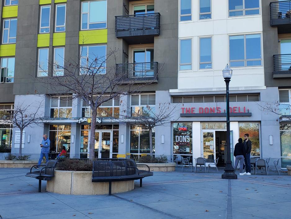 A photo of a plaza with seating near a mixed-use building with ground floor retail and apartments on top.