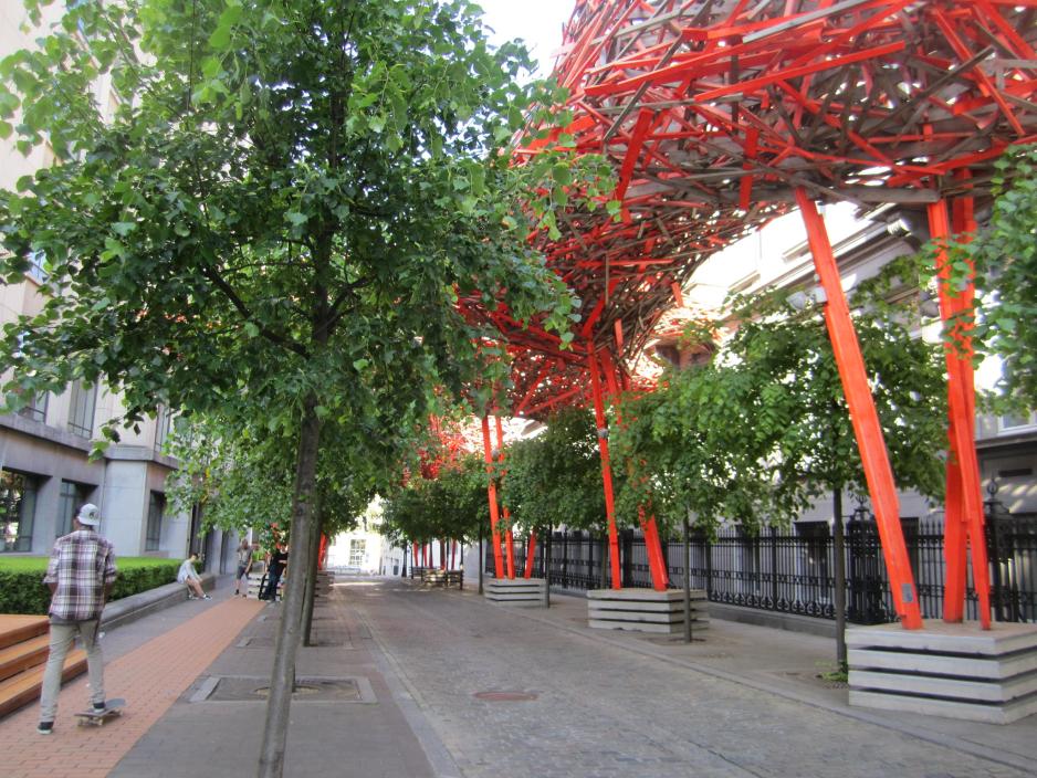 A photo of an open space between two buildings with trees and planter box seating.