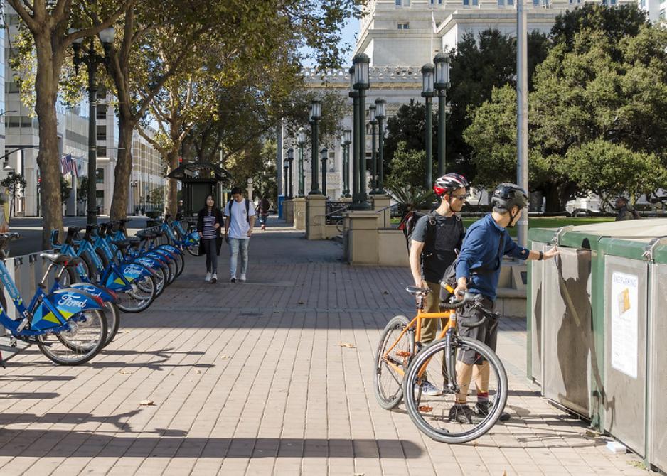 A photo of a bike share and bike storage on a sidewalk with people walking.