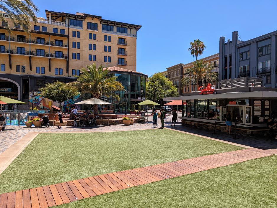 Photo of small park space surrounded by a playground, buildings, and trees