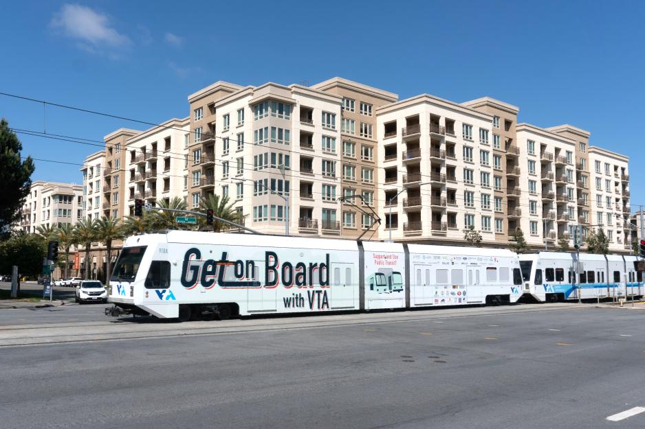 Photo of VA light rail traveling in front of a large multi family housing building