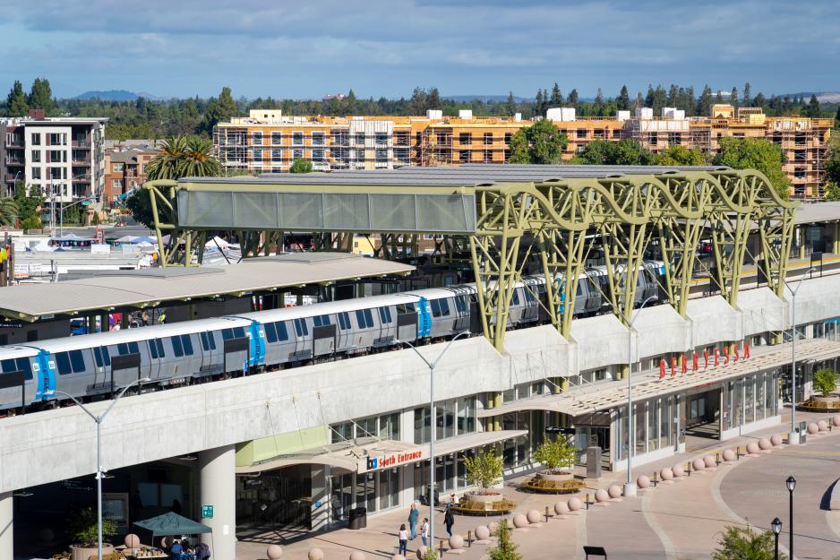 A photo of a BART train at the Berryessa transit center. In the distance is new construction.  