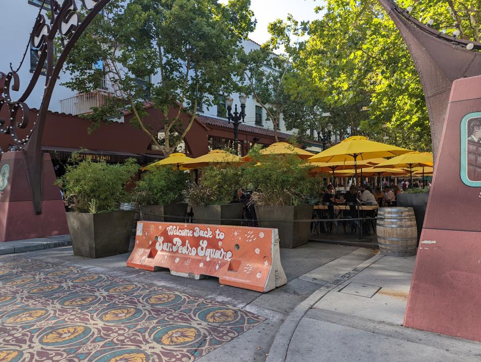 A photo of a closed street with a barrier with restaurant patio seating.