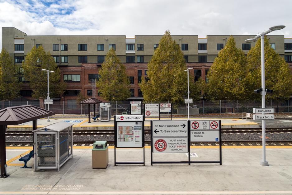 Photo of two train station platforms with signs and trees with a taller building in the background