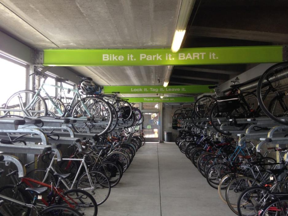 Photo of a bicycle parking room with bicycles parked on both sides of aisle in two levels with signs above