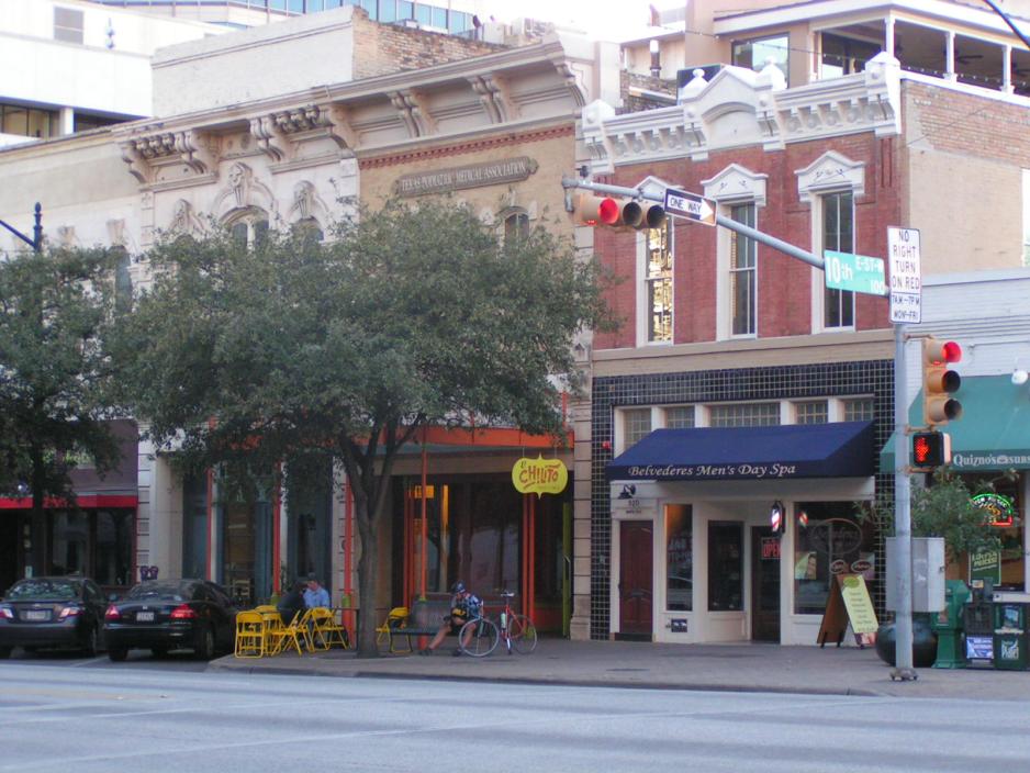 Photo of a series of two-story buildings with trees and people sitting in front