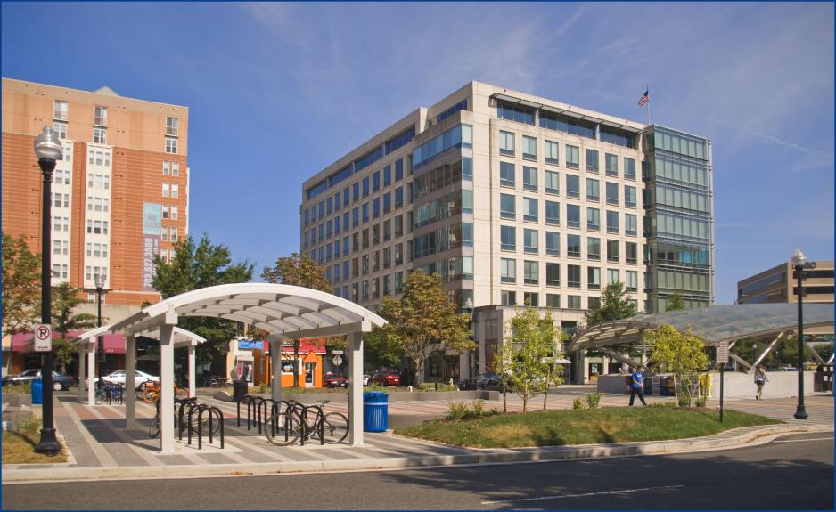 Photo of station plaza with covered bicycle parking and covered station entrance with buildings behind