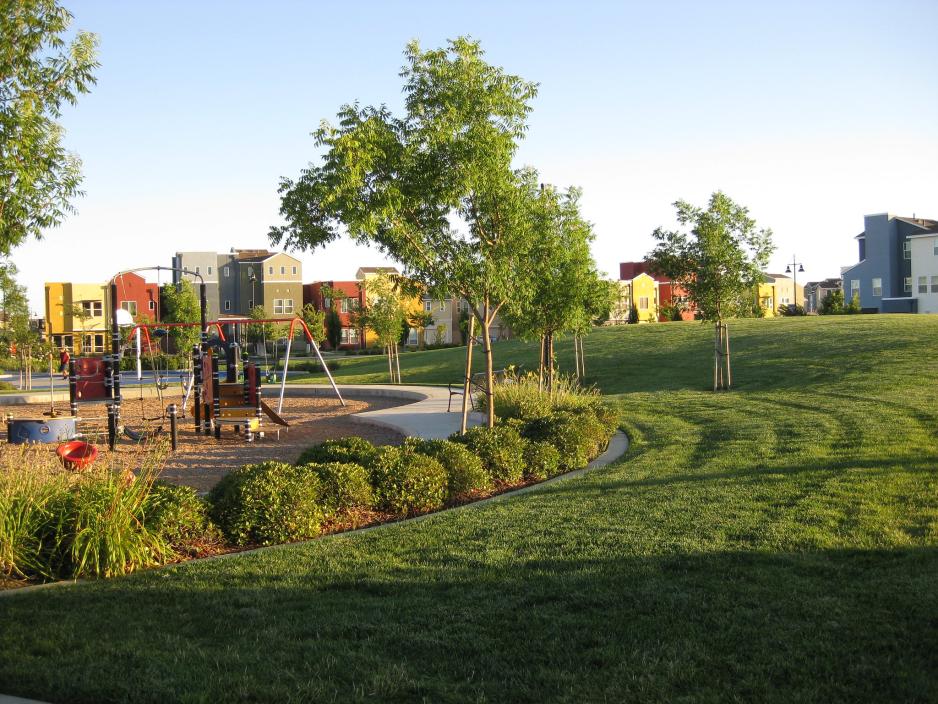 Photo of playground next to grassy area with trees and apartment buildings in the background