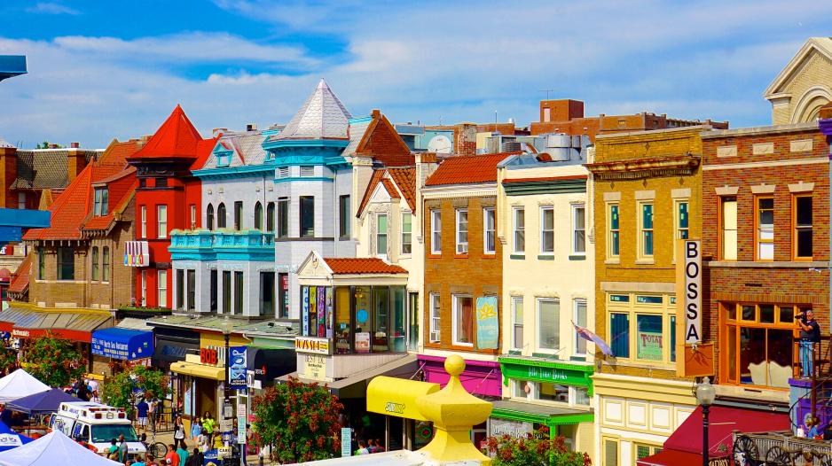 Photo of a row of colorful four story buildings with people walking in front