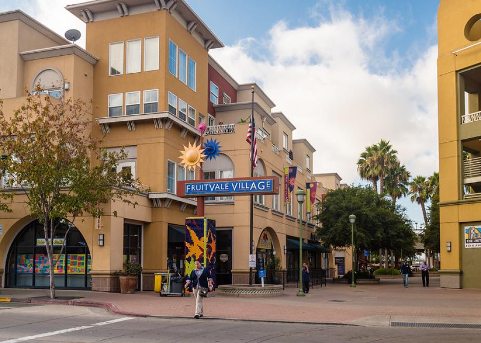 Photo of entrance to Fruitvale Village with two buildings surrounding pedestrian walkway with trees and people walking