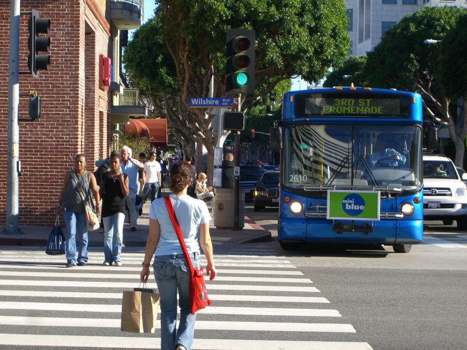 A photo of people walking on a crosswalk in a commercial corridor. 