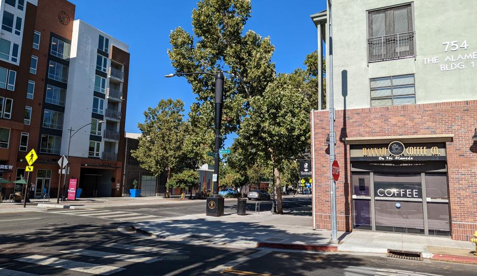 Photo of a street with taller buildings on both sides with ground-floor retail shops and residential apartments above on a sunny day