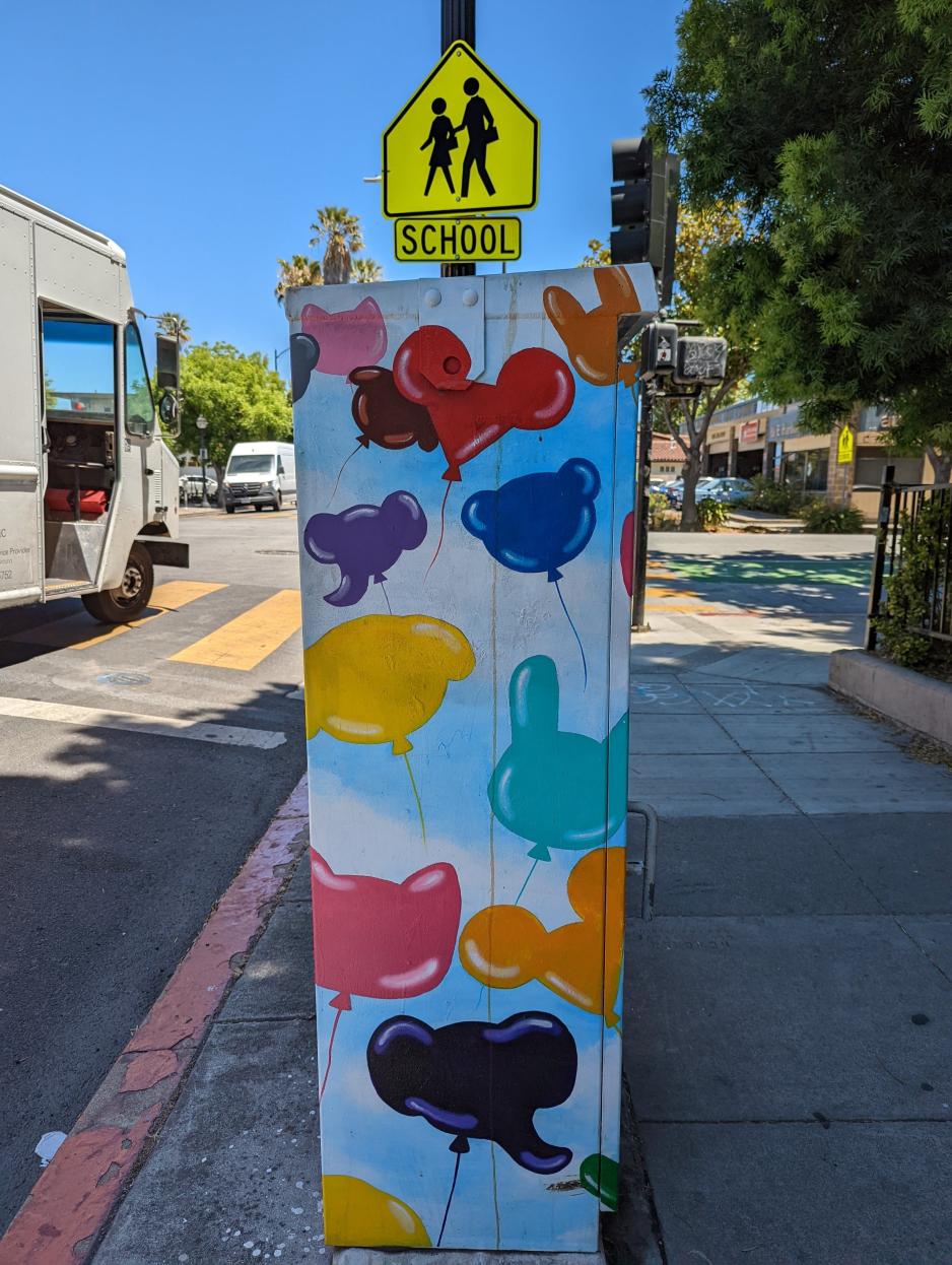 Photo of a utility box on the sidewalk that's painted with Mickey Mouse balloons of various colors