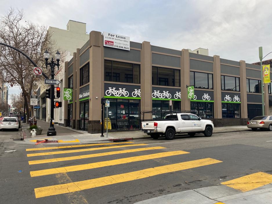 Photo of the outside of a grey building that provides bicycle parking with green and back signs 