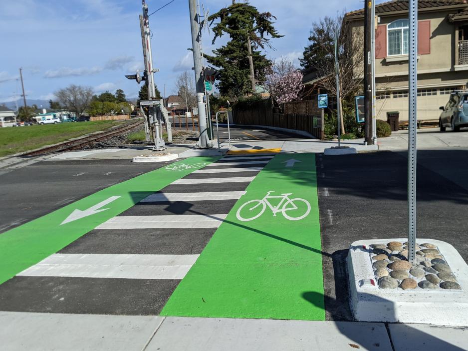 Photograph of a roadway crossing striped to provide a white pedestrian crossing and a green bike crossing.
