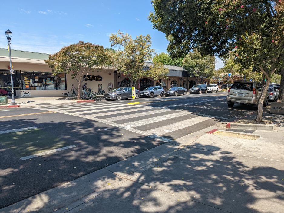 Photograph of a high visibility pedestrian crossing on a two lane road traveling through in a commercial area.