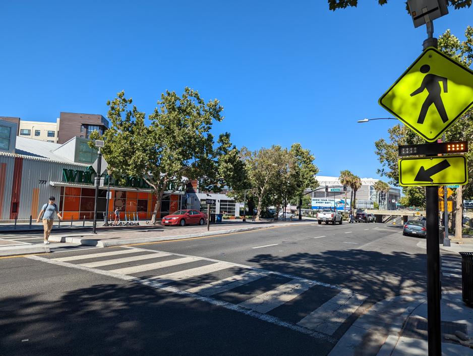 Photo of a pedestrian crossing a multi use street supported by a high-visibility crosswalk and flashing beacon.