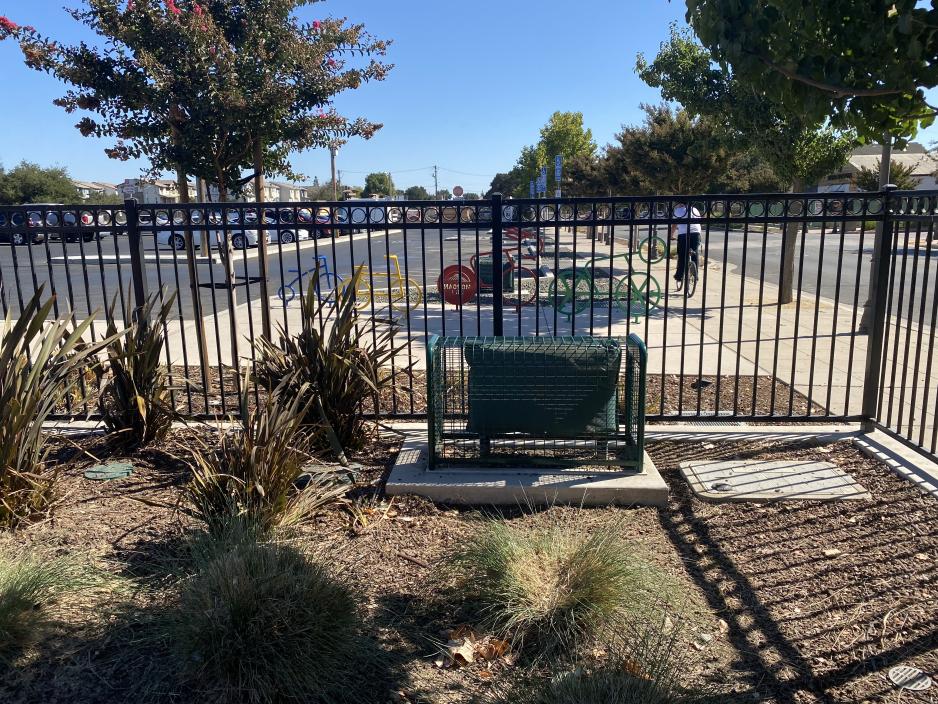 Photo of irrigation equipment behind a fence painted in green and covered by green wire to blend with surrounding landscaping