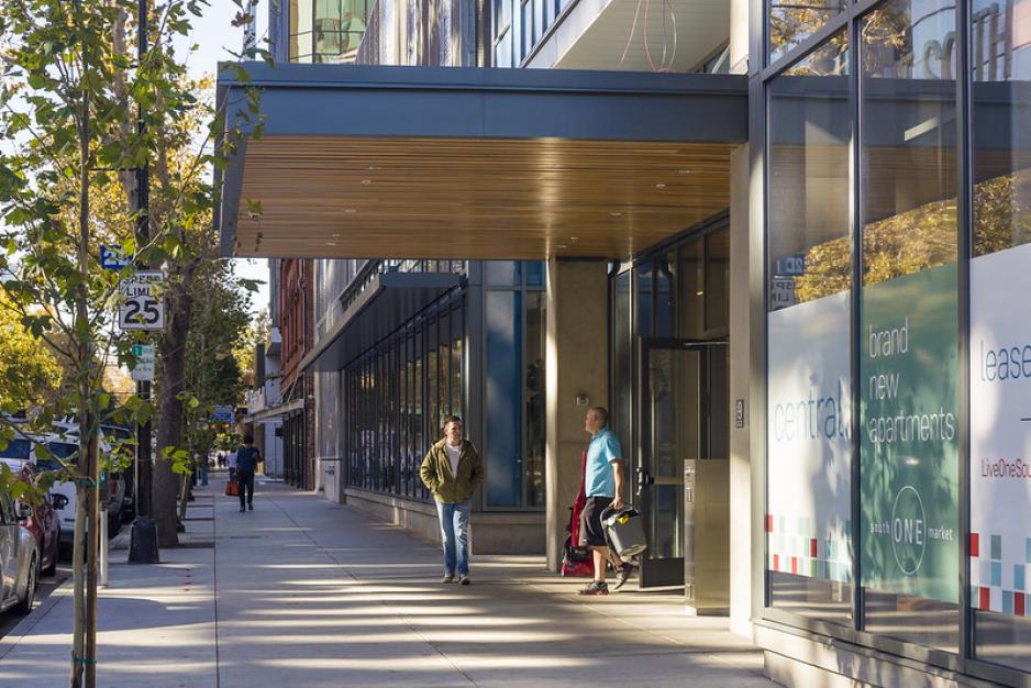 Photo of two men walking under an awning for an entrance of a building with trees on the side