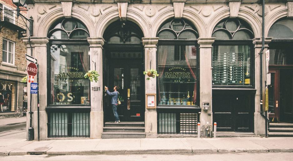 Photo of a restaurant on the bottom floor of a building with large arched windows and a person standing at the entrance