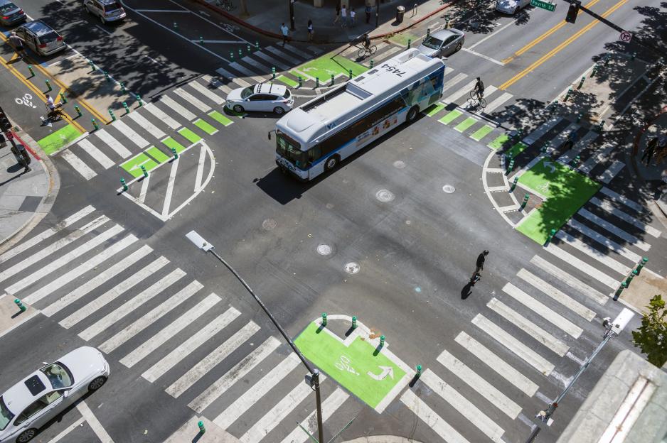 Photo of an intersection taken from above with a bus, several bicyclists, and cars traveling through
