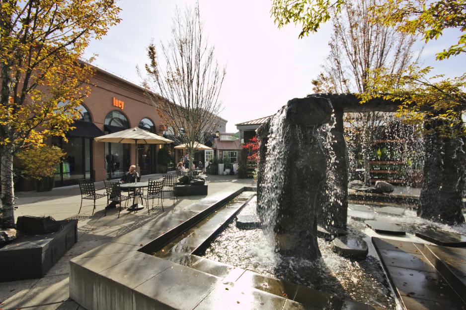Photo of a fountain in a shopping center with bistro tables and trees nearby